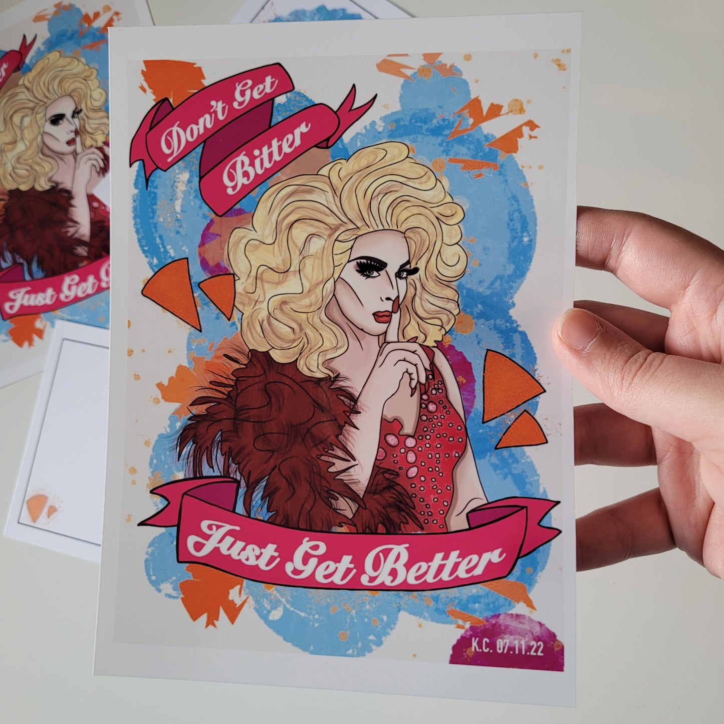 hand holding print of Alyssa Edwards. The tect reads "Don't get Bitter, Just get better" on pink banners.