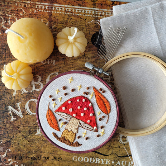 fall mushroom hoop resting on fabric embroideyr hoop and embroiery needles