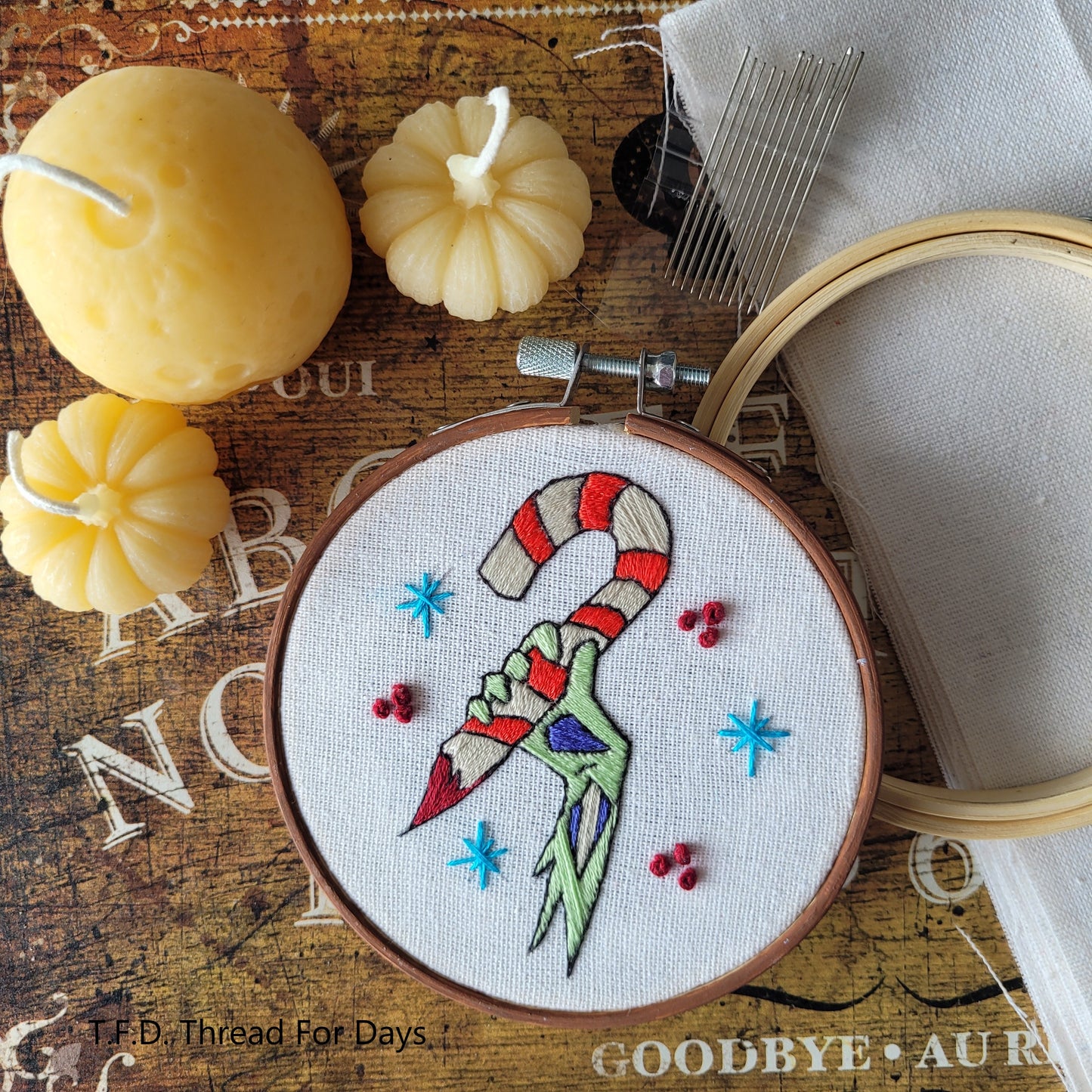 Zombie arm christmas hoop resting on fabric 4inch bamboo hoop and embroidery needles