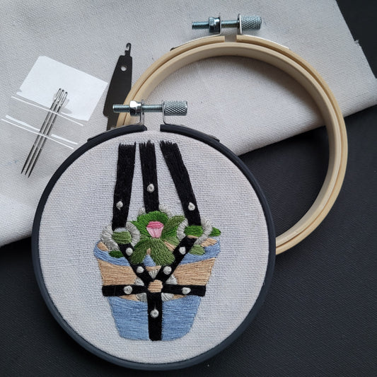 embroidery hoop of a succulent in a terracotta pot hanging in a BDSM harness