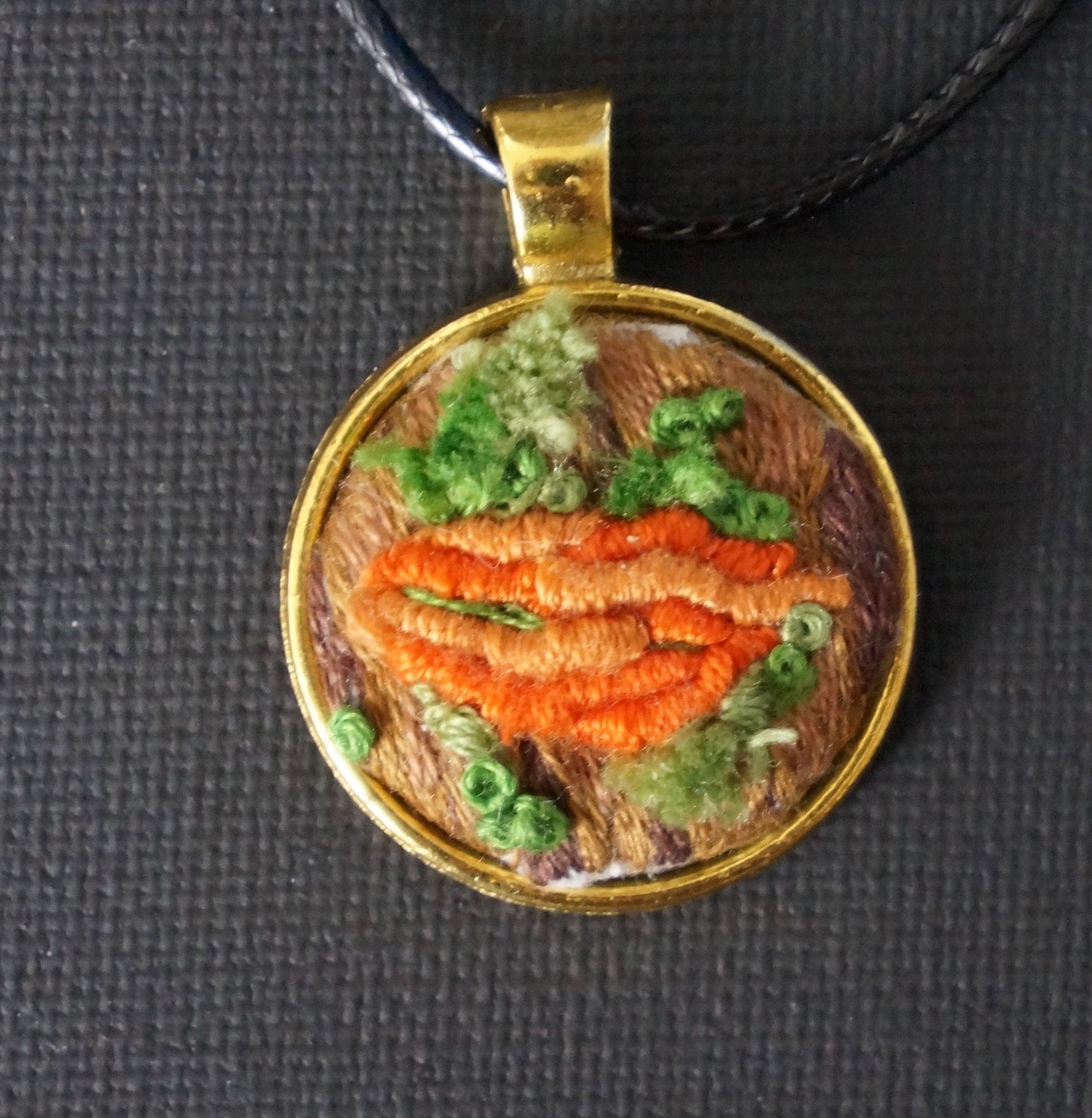 embroidered pendant featuring an orange bullion knot fungus with turkey work green moss set on an embroidered tree trunk