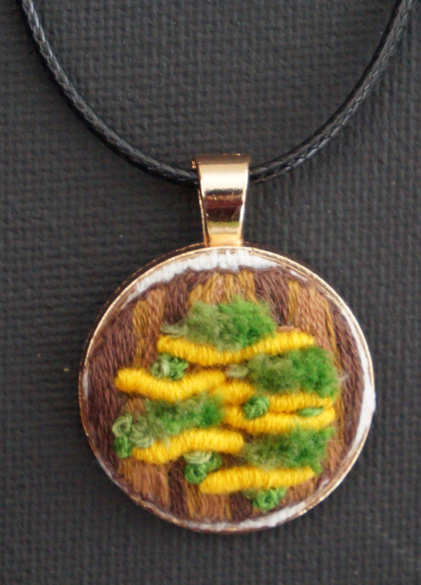 embroidered pendant featuring an yellow bullion knot fungus with turkey work green moss set on an embroidered tree trunk