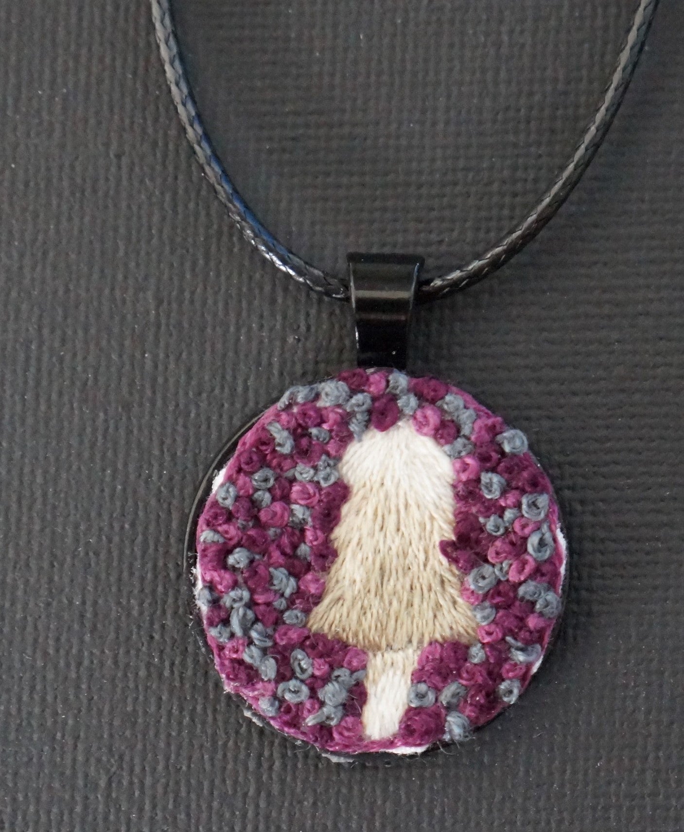 a shaggy off shite lions mane mushroom embroidered pendant with a purple and grey textured french knot background