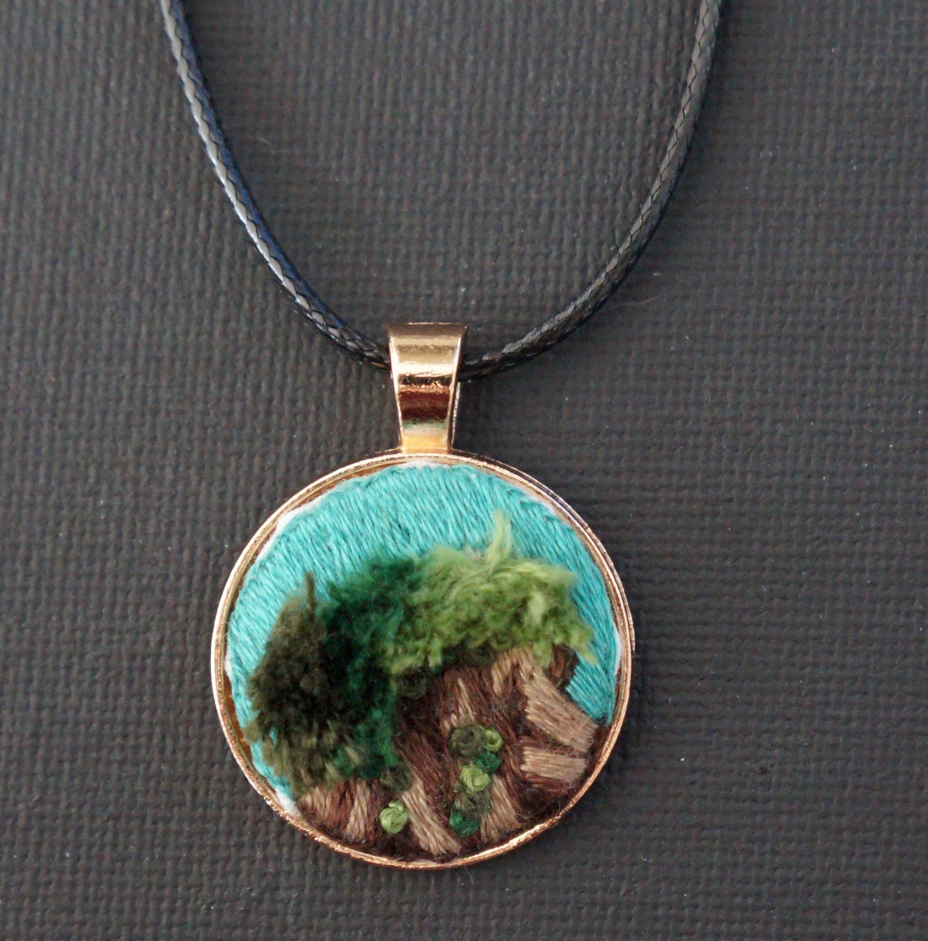 an embroidered pendant featuring a mossy stump. The moss is done in textured green turkey work.