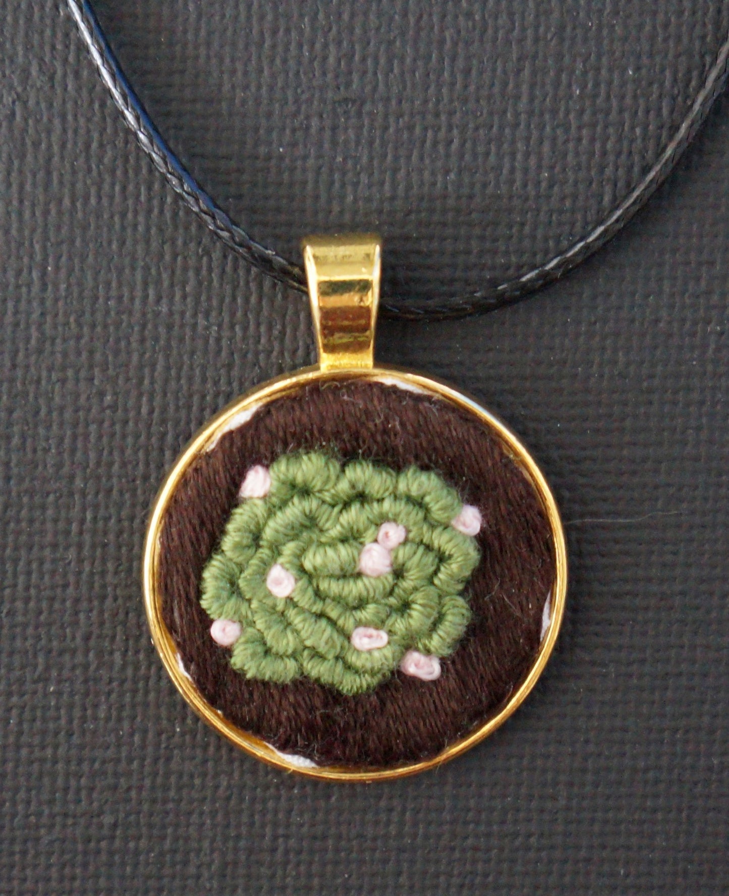 an embroidered pendant with a bullion knot succulent with pink french knot flowers. 