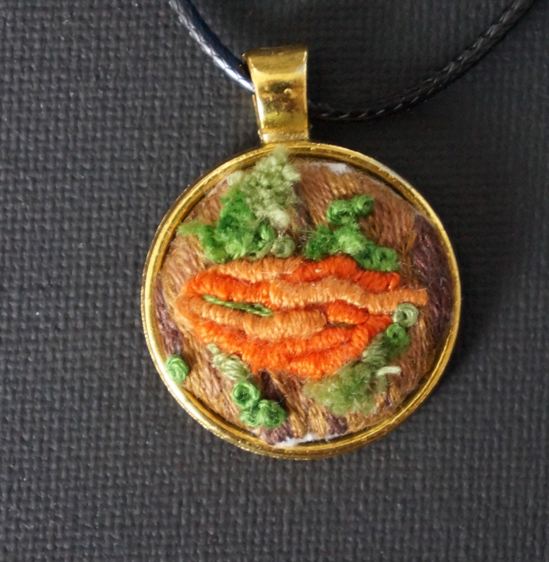 embroidered pendant featuring an orange bullion knot fungus with turkey work green moss set on an embroidered tree trunk 